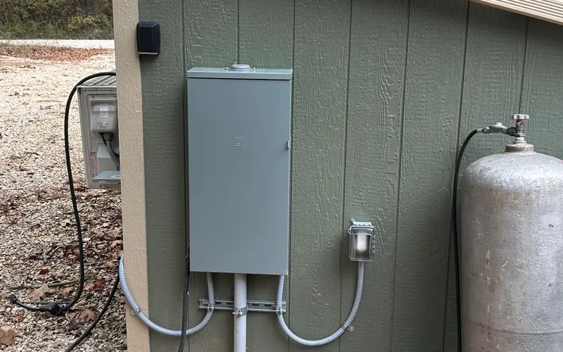 Exterior electrical panel with its cover installed and conduit on an outbuilding.